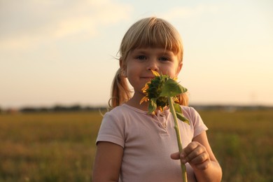 Photo of Cute little girl with sunflower at meadow. Child enjoying beautiful nature