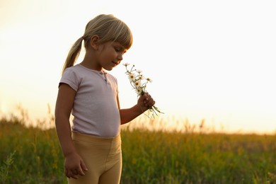 Photo of Cute little girl with chamomiles at meadow, space for text. Child enjoying beautiful nature