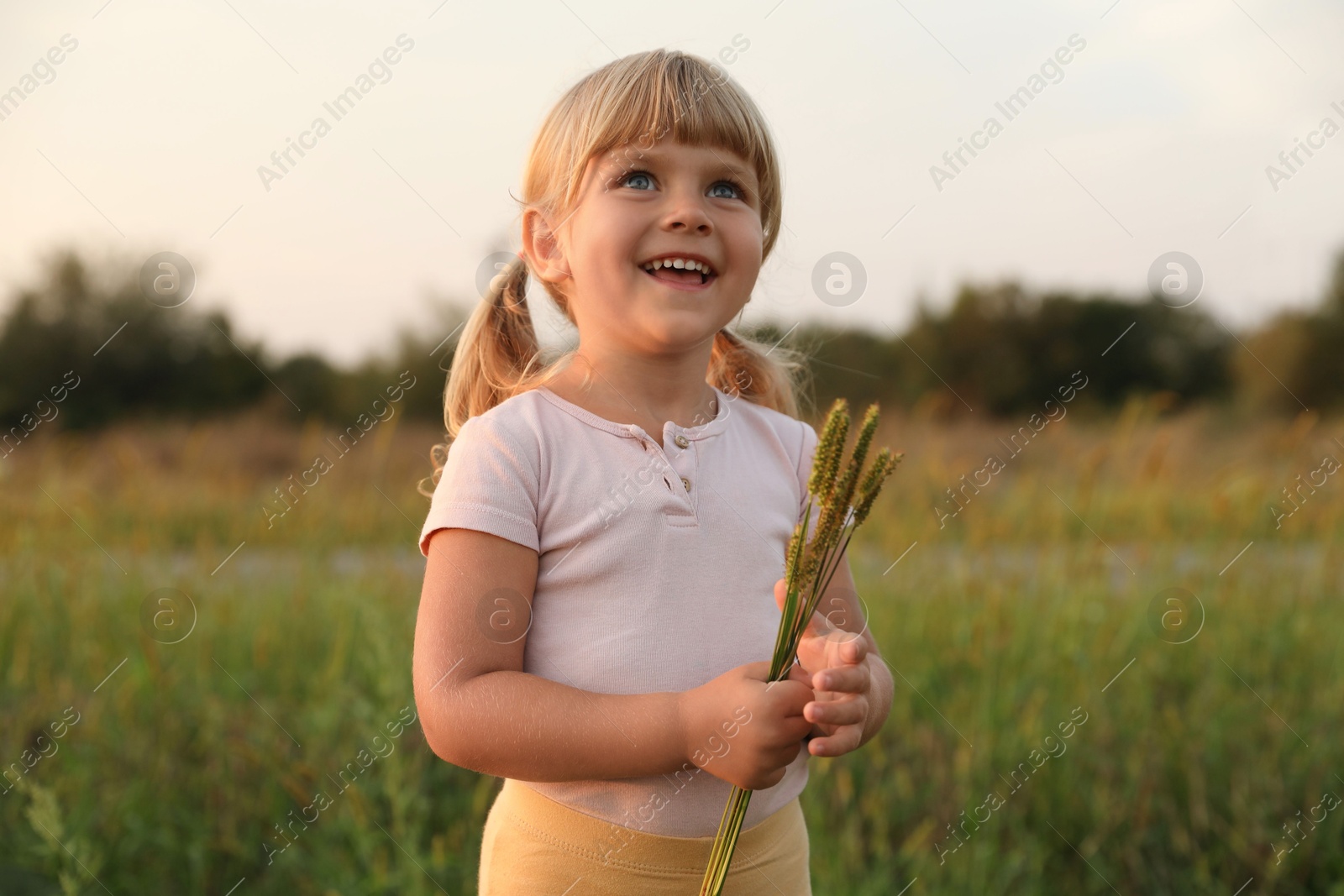 Photo of Cute little girl with plants at meadow. Child enjoying beautiful nature