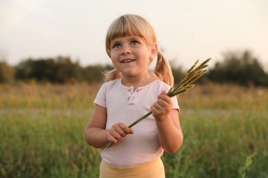 Photo of Cute little girl with plants at meadow. Child enjoying beautiful nature