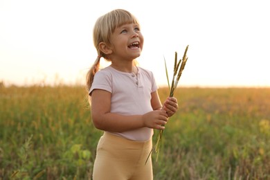 Photo of Cute little girl with plants at meadow. Child enjoying beautiful nature