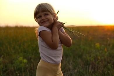 Cute little girl with plants at meadow. Child enjoying beautiful nature