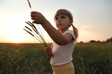 Cute little girl with plants at meadow. Child enjoying beautiful nature