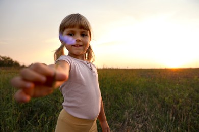 Cute little girl with flower outdoors at sunset, space for text. Child enjoying beautiful nature