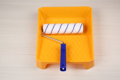 Paint roller and tray on light wooden table, above view