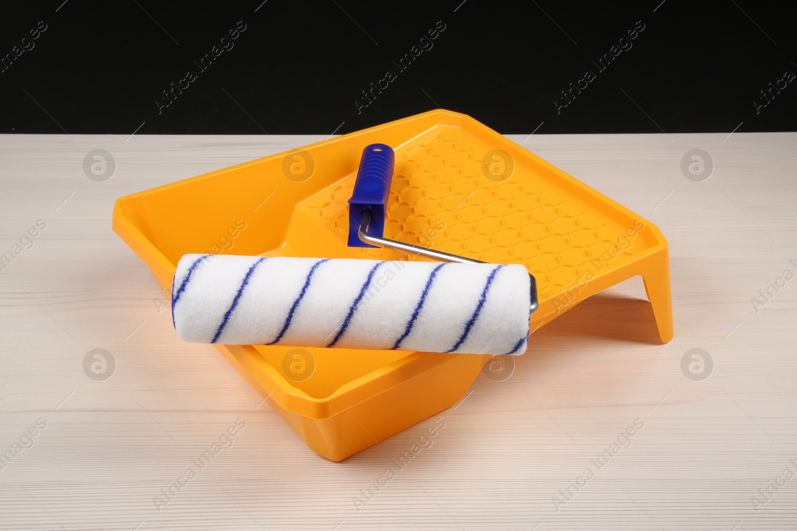 Photo of Paint roller and tray on light wooden table against black background