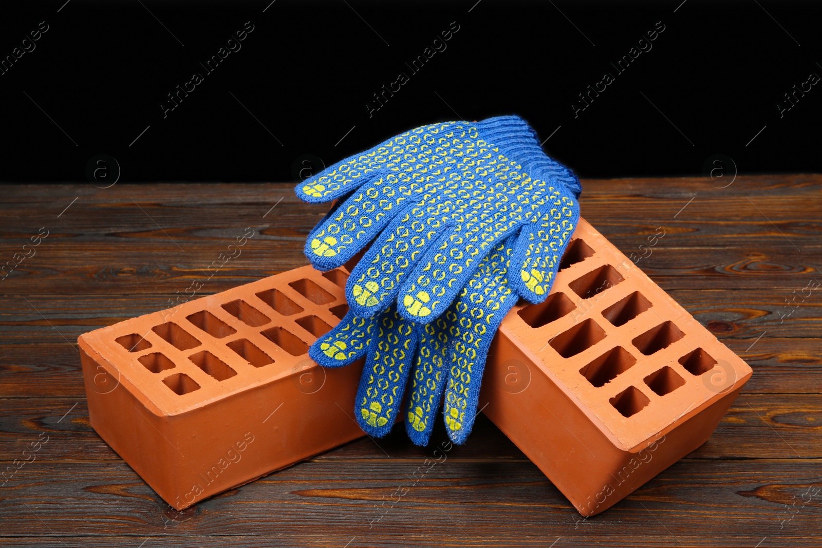 Photo of Red bricks and rubber gloves on wooden table. Building material