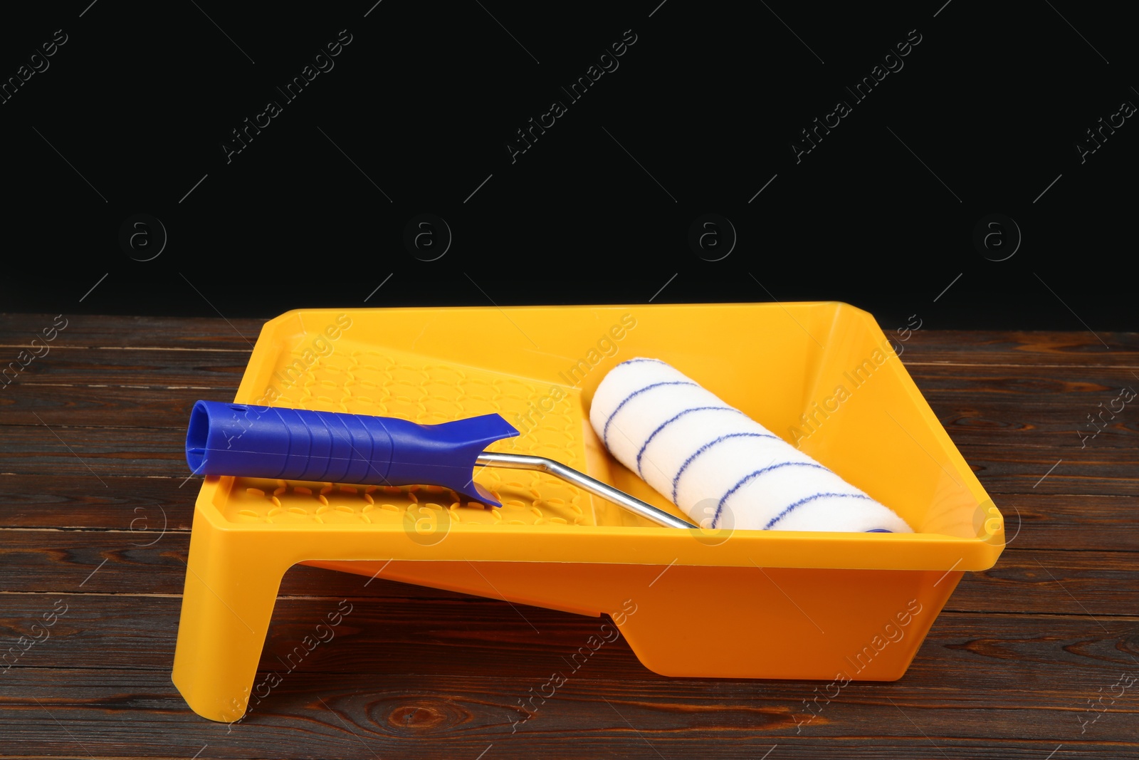 Photo of Tray and paint roller on wooden table. Construction tools