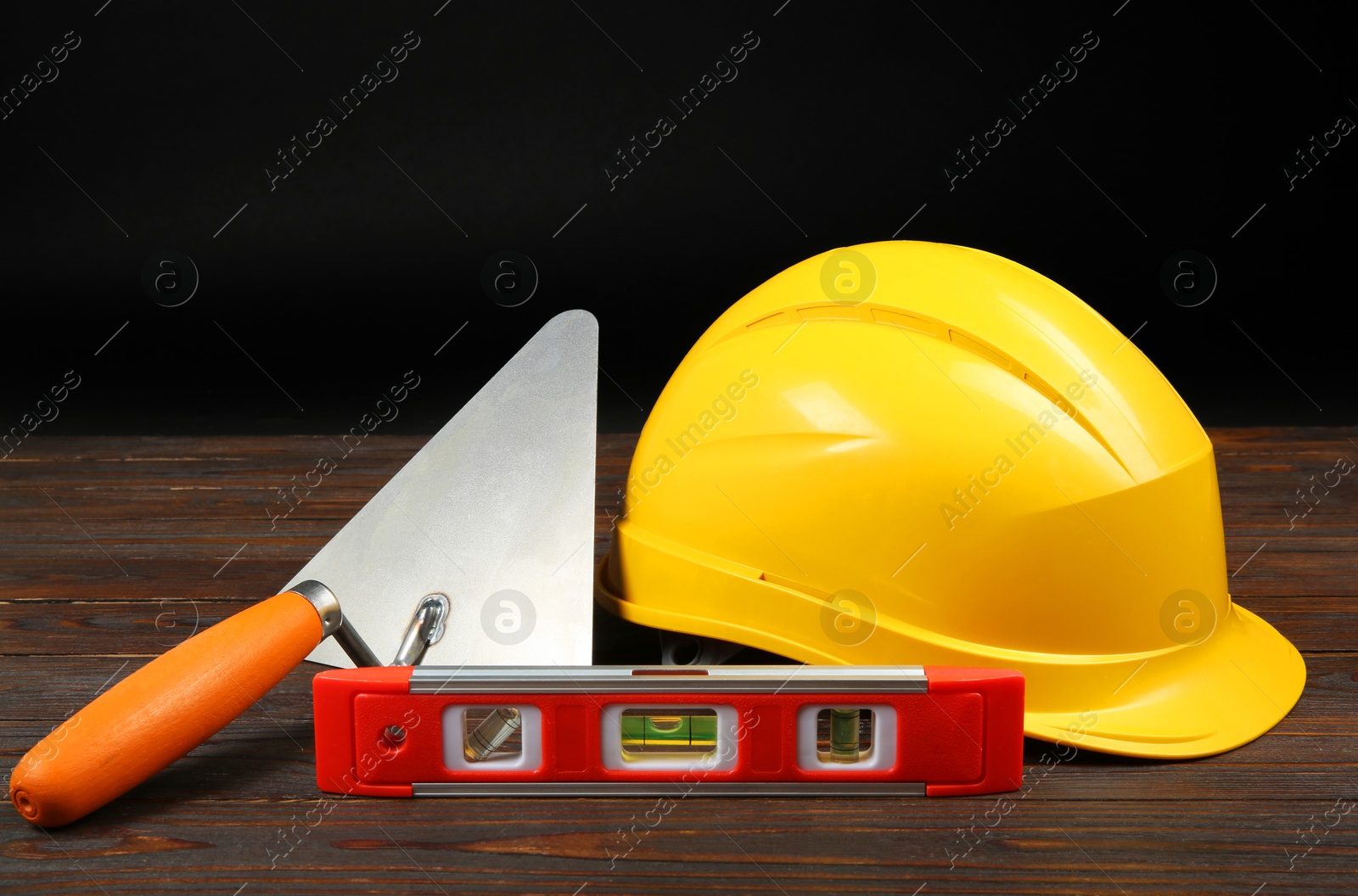 Photo of Yellow hard hat, putty knife and spirit level on wooden table