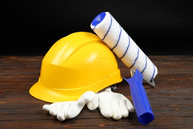 Photo of Yellow hard hat, paint roller and rubber gloves on wooden table