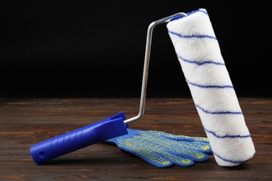 Photo of Paint roller and rubber glove on wooden table, closeup