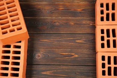 Many red bricks on wooden table, flat lay with space for text. Building material