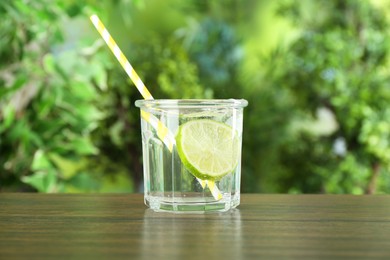 Photo of Glass of soda water with lime on wooden table against blurred background