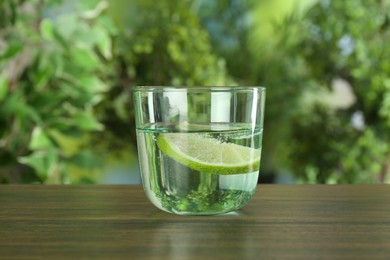 Photo of Glass of soda water with lime on wooden table against blurred background