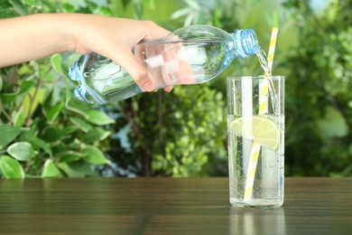 Photo of Woman pouring soda water from bottle into glass at wooden table, closeup