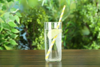 Photo of Glass of soda water with lime on wooden table against blurred background