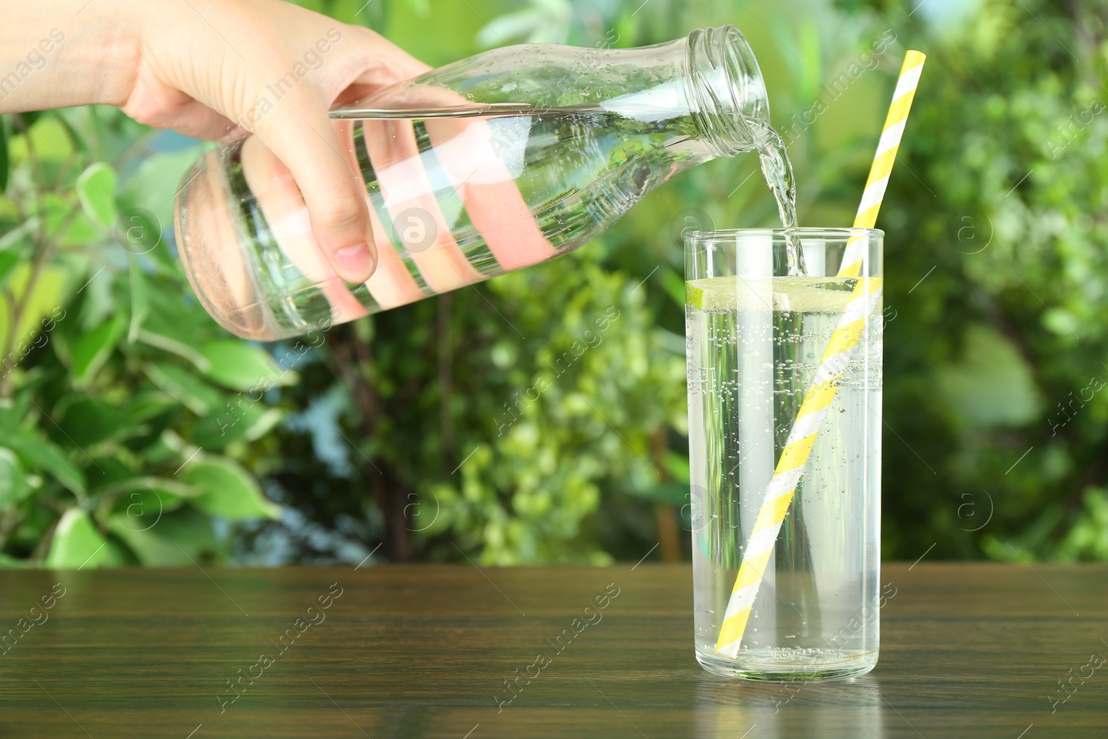 Photo of Woman pouring soda water from bottle into glass at wooden table, closeup