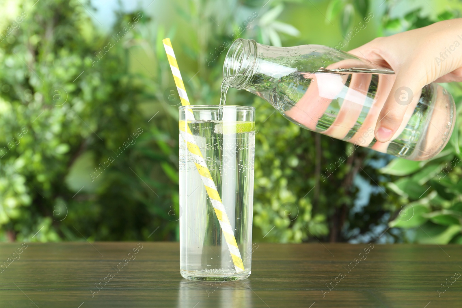 Photo of Woman pouring soda water from bottle into glass at wooden table, closeup