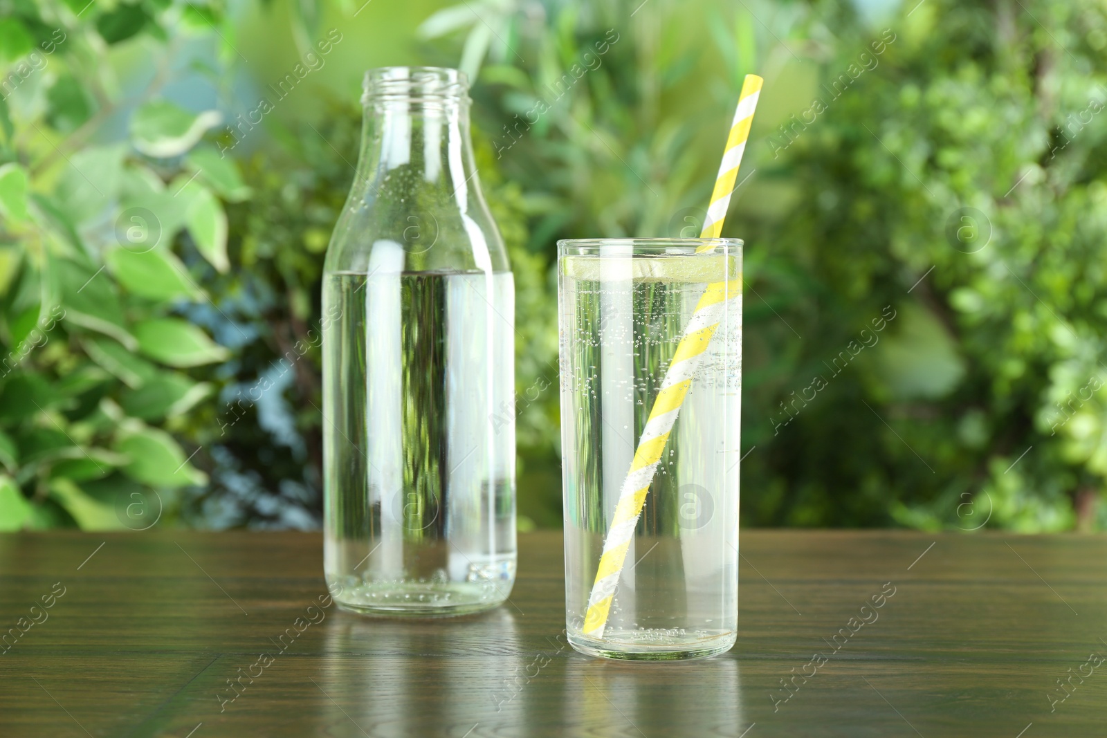 Photo of Glass and bottle of soda water with lime on wooden table against blurred background