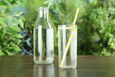 Photo of Glass and bottle of soda water with lime on wooden table against blurred background