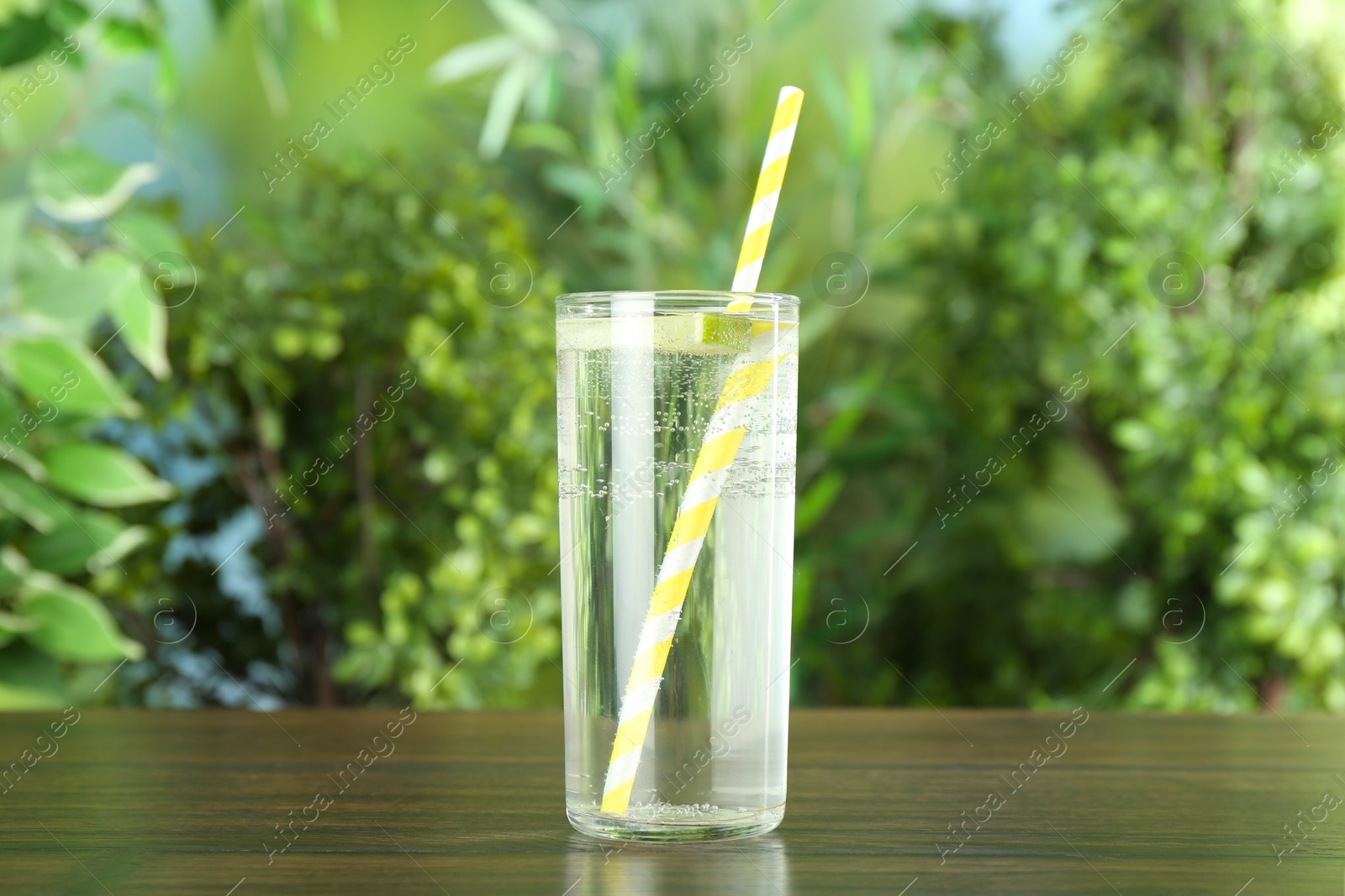 Photo of Glass of soda water with lime on wooden table against blurred background