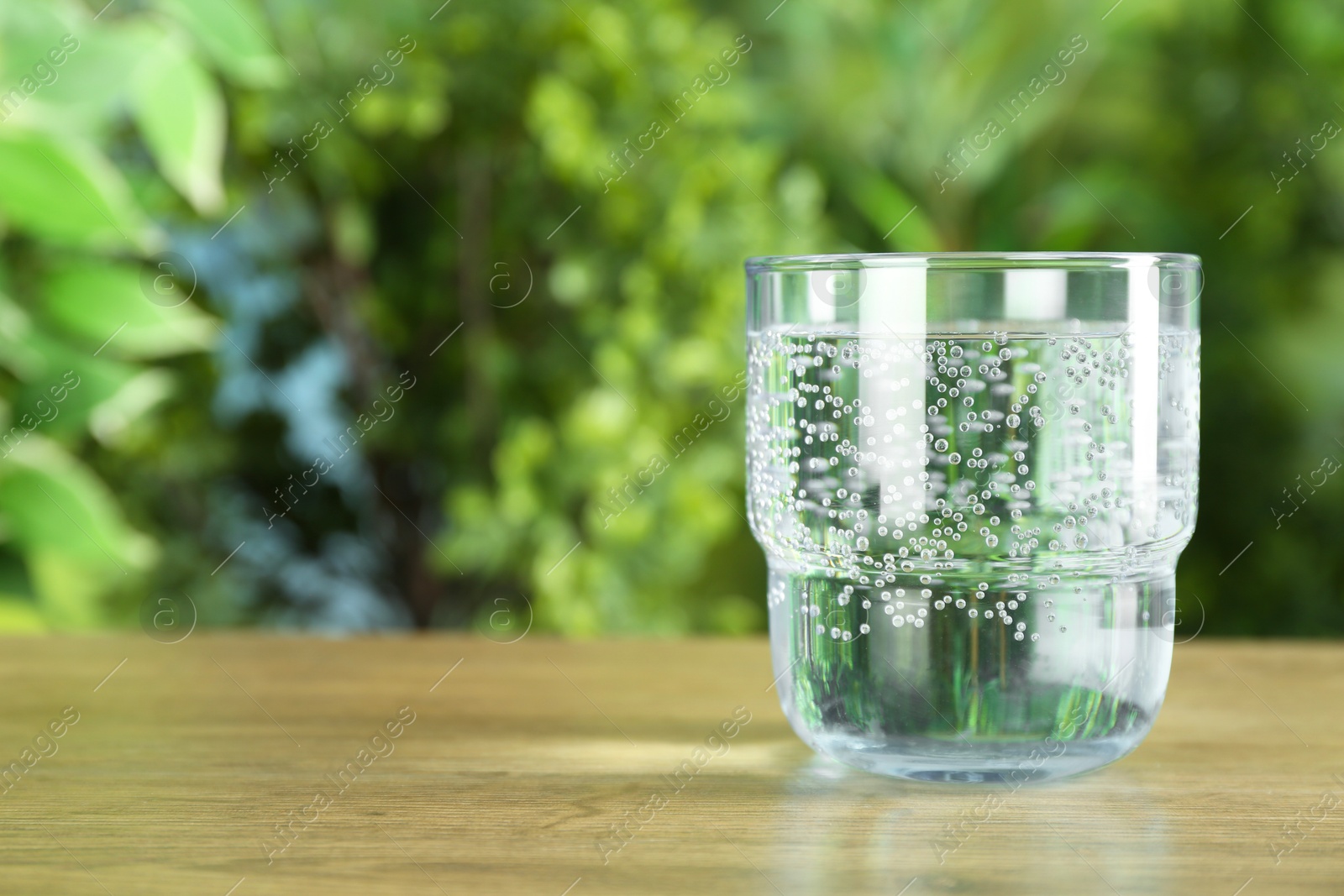 Photo of Glass of soda water on wooden table against blurred background. Space for text