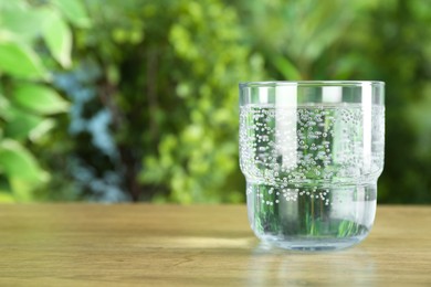 Photo of Glass of soda water on wooden table against blurred background. Space for text