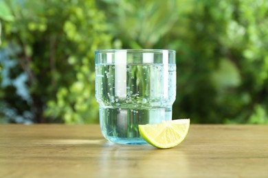 Photo of Glass of soda water with lime on wooden table against blurred background