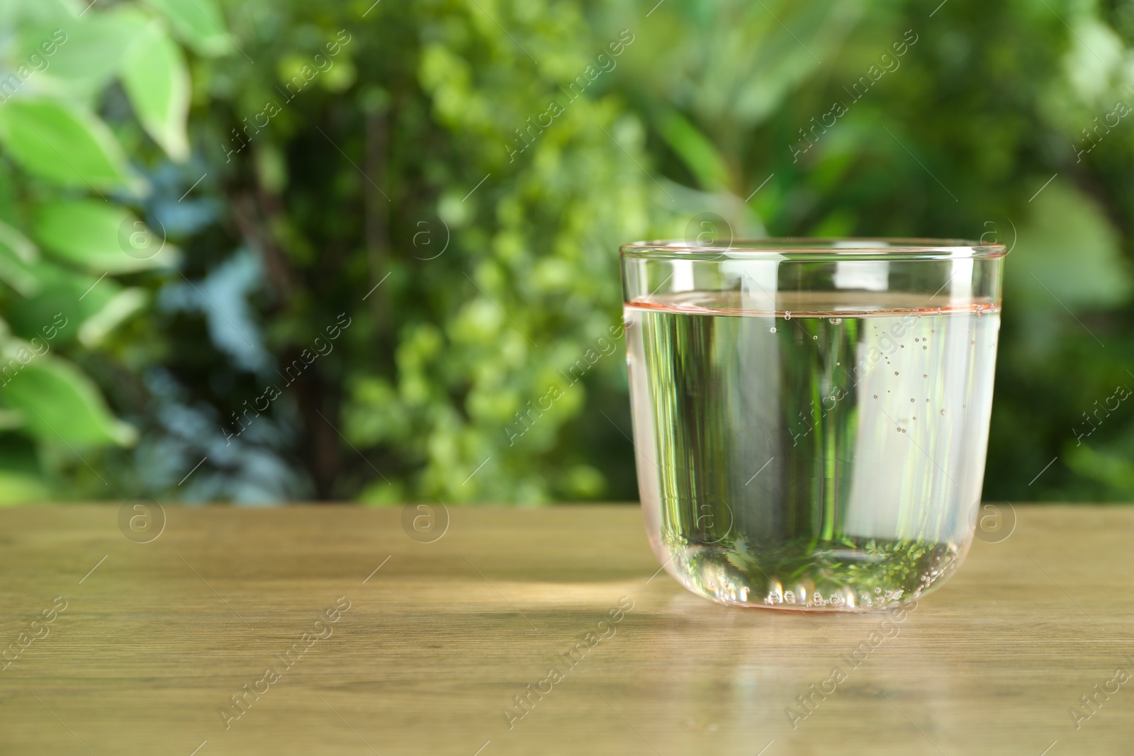 Photo of Glass of soda water on wooden table against blurred background. Space for text