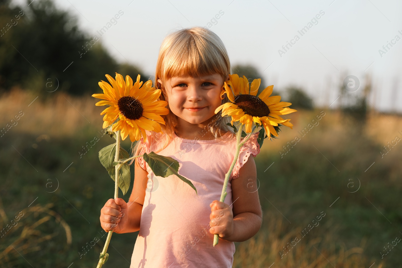 Photo of Little girl with sunflowers at meadow. Child enjoying beautiful nature