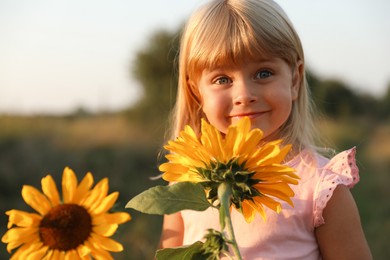 Little girl with sunflowers at meadow. Child enjoying beautiful nature