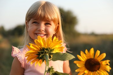 Photo of Little girl with sunflowers at meadow. Child enjoying beautiful nature