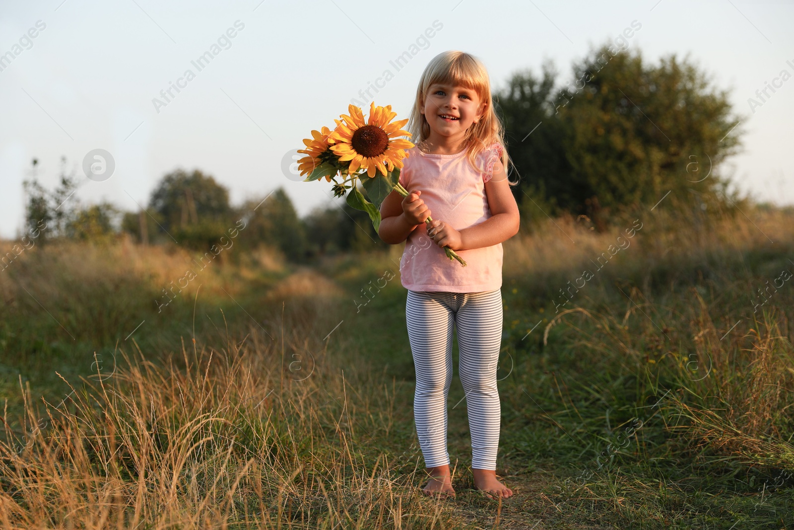 Photo of Little girl with sunflowers at meadow. Child enjoying beautiful nature