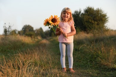 Photo of Little girl with sunflowers at meadow. Child enjoying beautiful nature