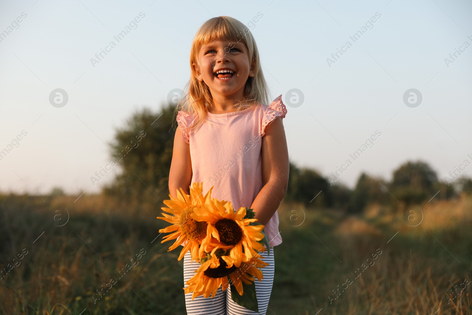 Photo of Little girl with sunflowers at meadow. Child enjoying beautiful nature