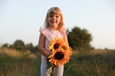 Little girl with sunflowers at meadow. Child enjoying beautiful nature