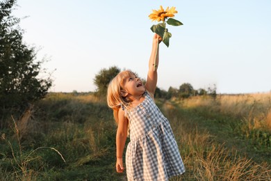 Little girl with sunflower at meadow. Child enjoying beautiful nature