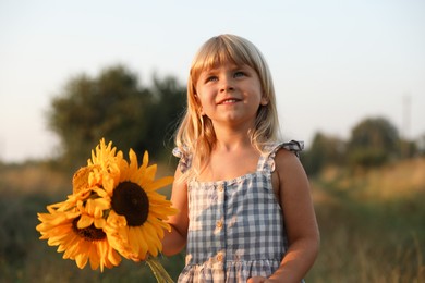 Photo of Little girl with sunflowers at meadow. Child enjoying beautiful nature