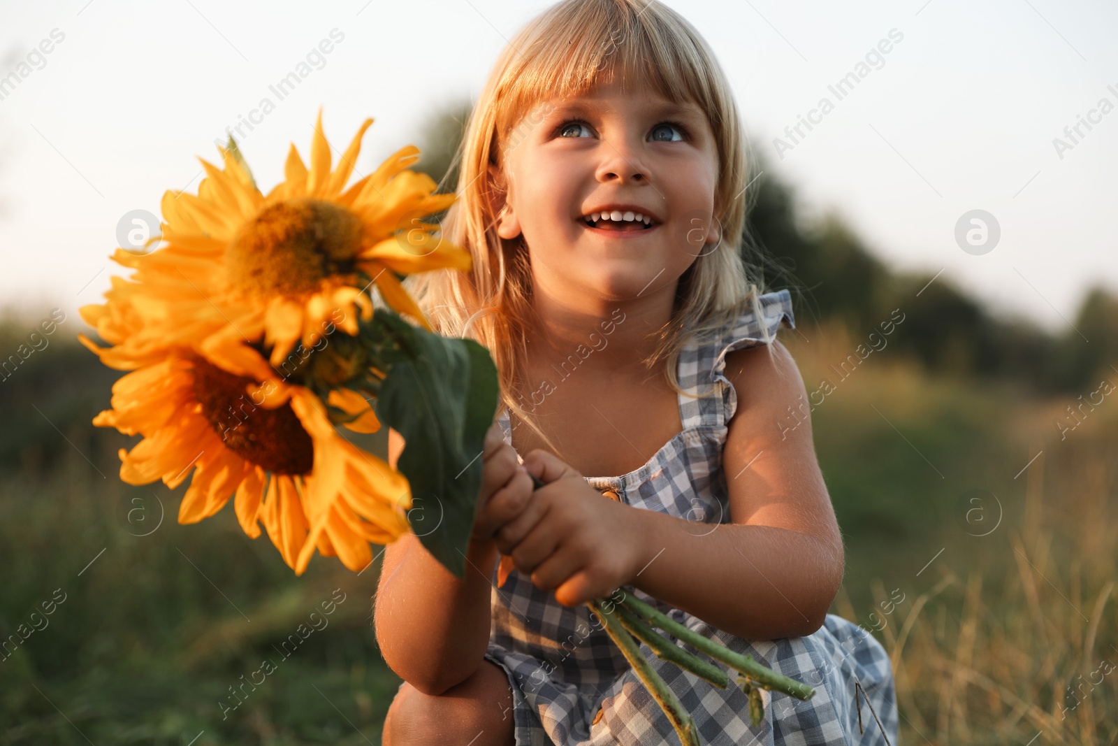 Photo of Little girl with sunflowers at meadow. Child enjoying beautiful nature