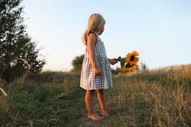 Little girl with sunflowers at meadow. Child enjoying beautiful nature