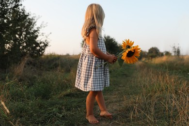 Photo of Little girl with sunflowers at meadow. Child enjoying beautiful nature