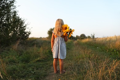 Photo of Little girl with sunflowers at meadow, back view. Child enjoying beautiful nature