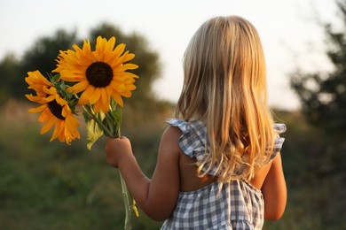 Photo of Little girl with sunflowers at meadow, back view. Child enjoying beautiful nature