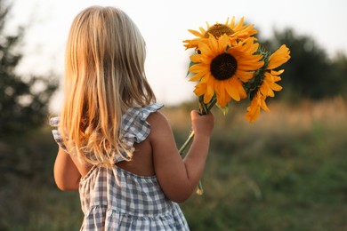 Photo of Little girl with sunflowers at meadow, back view. Child enjoying beautiful nature