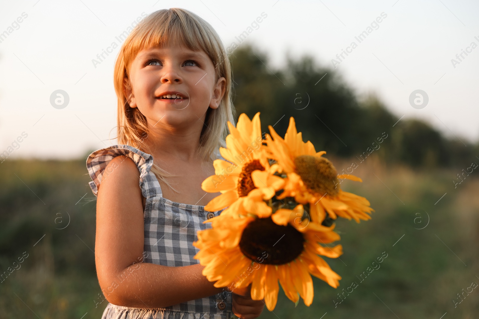 Photo of Little girl with sunflowers at meadow. Child enjoying beautiful nature