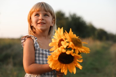 Photo of Little girl with sunflowers at meadow. Child enjoying beautiful nature