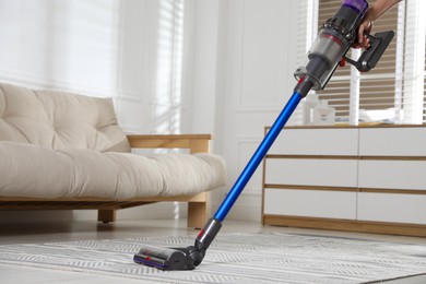 Photo of Woman cleaning carpet with cordless vacuum cleaner indoors, closeup