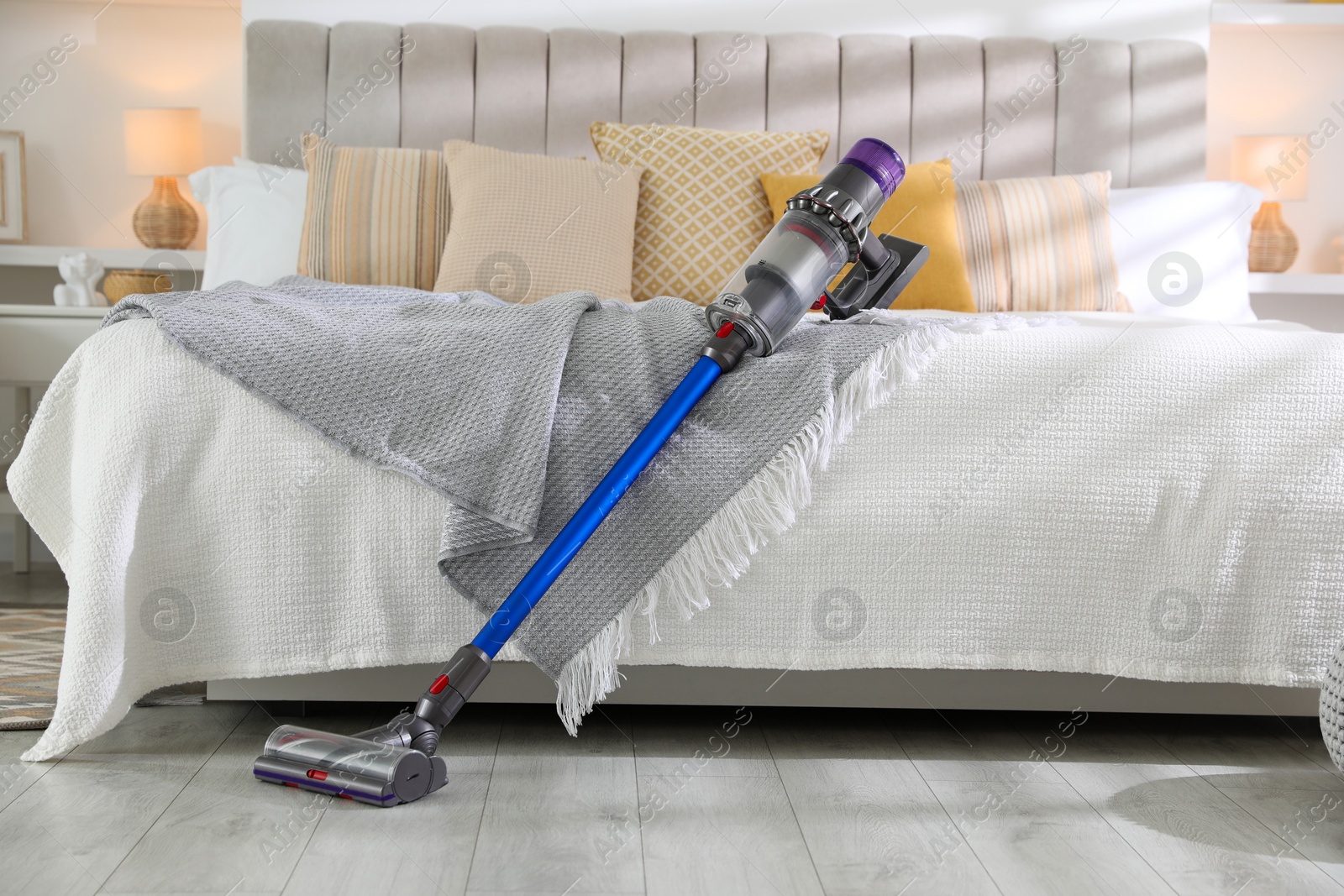 Photo of One cordless vacuum cleaner leaning on bed indoors