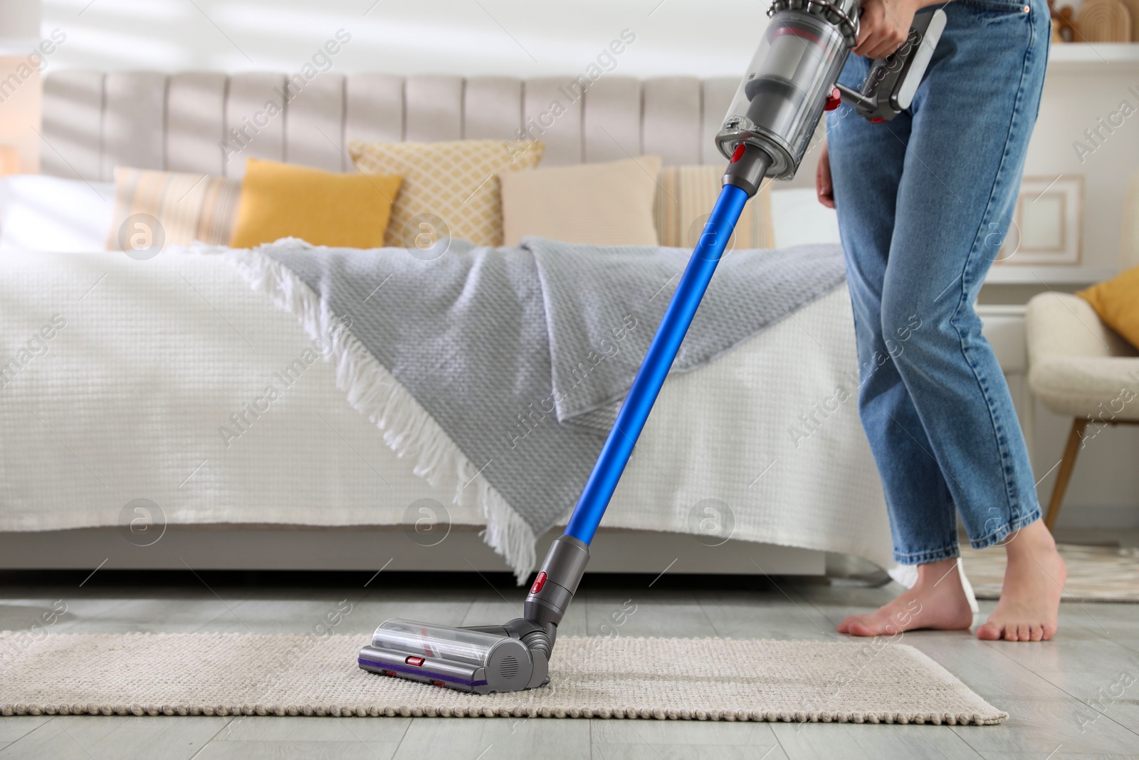 Photo of Woman cleaning rug with cordless vacuum cleaner indoors, closeup. Space for text