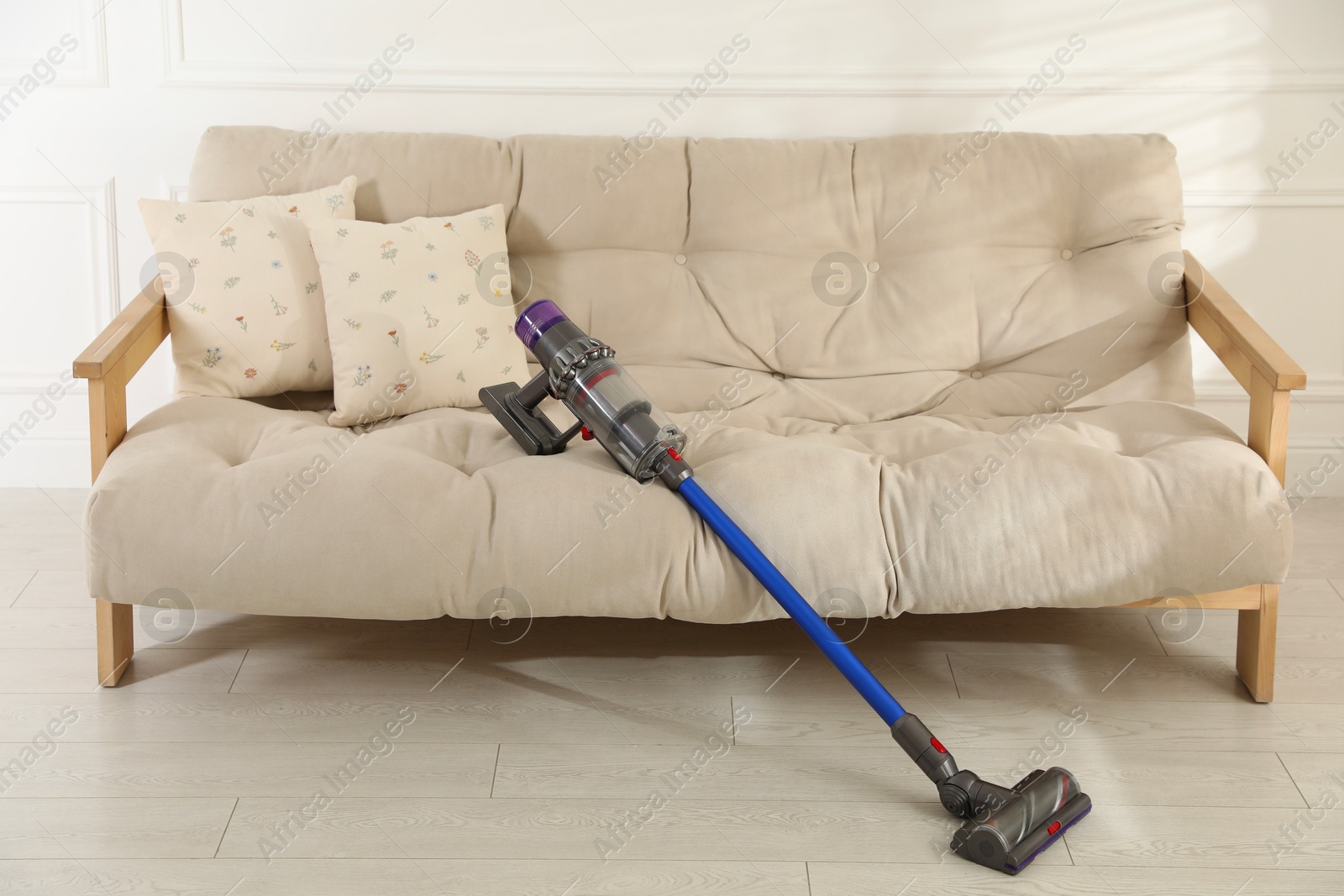 Photo of One cordless vacuum cleaner leaning on sofa indoors